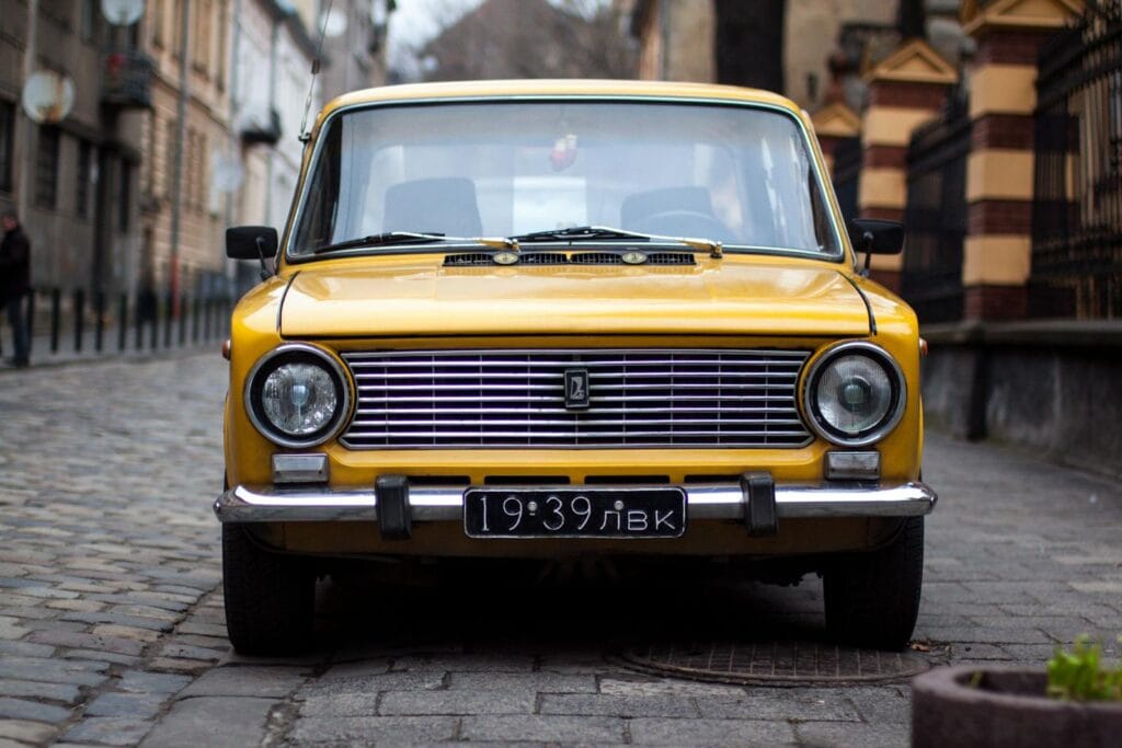 Front view of a vintage yellow car parked on a cobblestone street in Lviv, Ukraine.